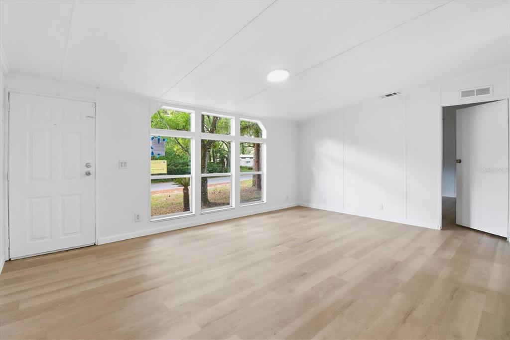 A bright, empty room features white walls, light wood-look flooring, and a large window wall — 2565 E NORTH STREET, INVERNESS, FL
