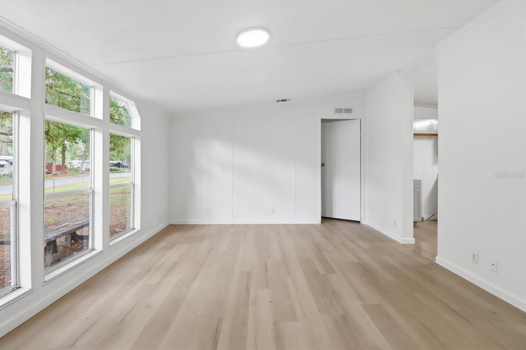 A bright, empty room features light wood-look flooring, white walls, and large windows — 2565 E NORTH STREET, INVERNESS, FL