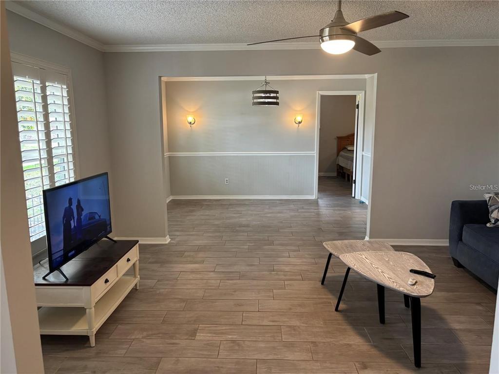 A living room with gray walls, wood-look tile flooring, a ceiling fan, and a television — 105 E COTTESMORE CIRCLE, LONGWOOD, FL