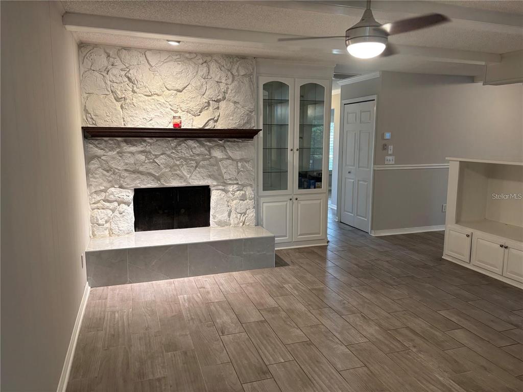 A living room features a white stone fireplace, built-in glass cabinets, and wood-look tile flooring — 105 E COTTESMORE CIRCLE, LONGWOOD, FL