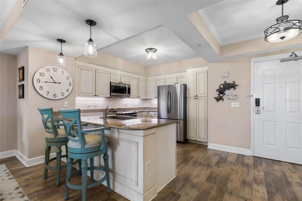 A kitchen features white cabinets, stainless steel appliances, a granite island, and two blue stools — 200 OCEAN CREST DRIVE UNIT 1016, PALM COAST, FL
