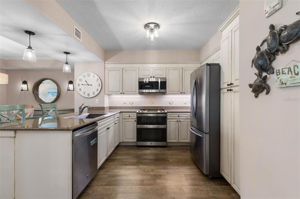 A kitchen features white cabinets, stainless steel appliances, granite countertops, and wood-look flooring — 200 OCEAN CREST DRIVE UNIT 1016, PALM COAST, FL
