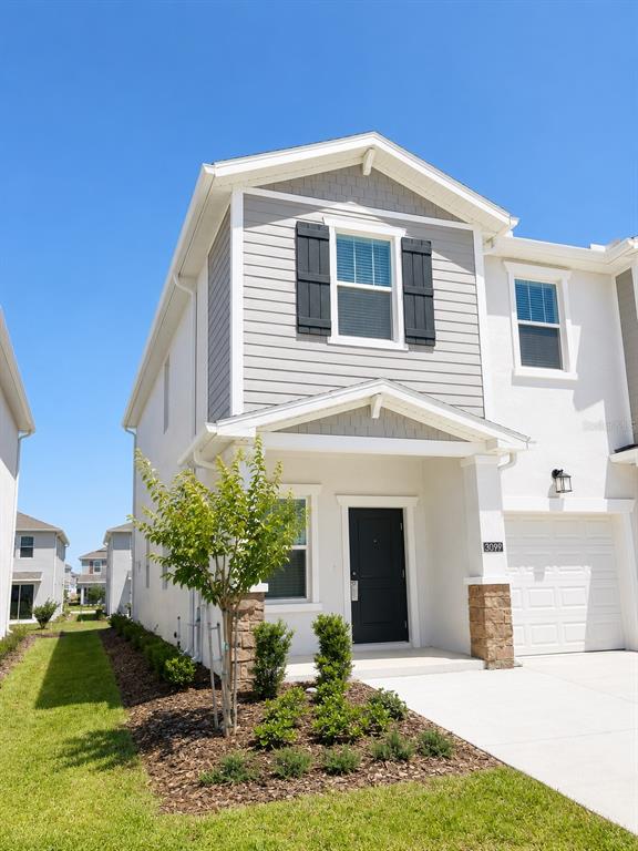 A two-story townhouse with a white stucco facade, gray siding, and a small front garden — 3099 MINDFULLNESS DRIVE, CLERMONT, FL