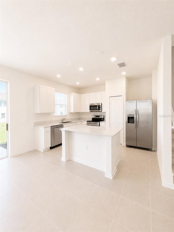A bright kitchen features white cabinetry, stainless steel appliances, and a central island — 3099 MINDFULLNESS DRIVE, CLERMONT, FL