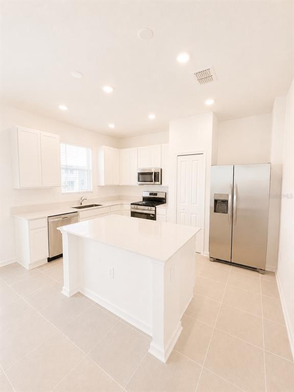 A kitchen features white cabinets, stainless steel appliances, a center island, and light-colored tile flooring — 3099 MINDFULLNESS DRIVE, CLERMONT, FL