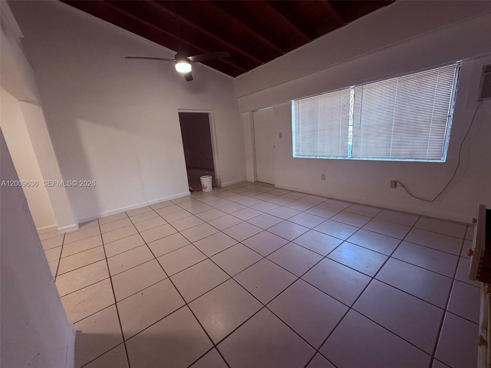 A room with white walls, light-colored floor tiles, a ceiling fan, and a large window — 590 NW 46th St # 2, Miami FL 33127, MIAMI, FL