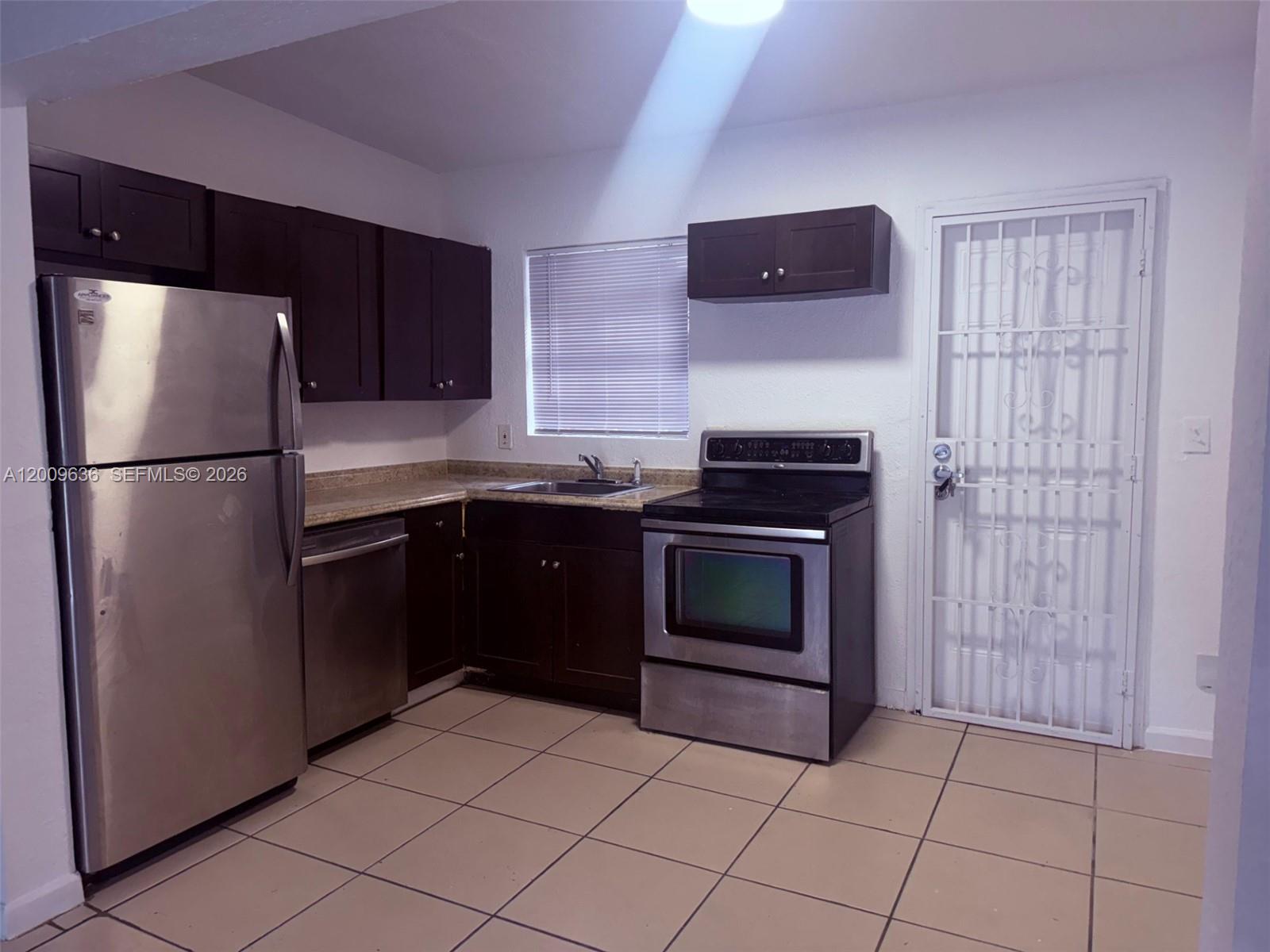 A kitchen features dark wood cabinets, stainless steel appliances, and light-colored floor tiles — 590 NW 46th St # 2, Miami FL 33127, MIAMI, FL
