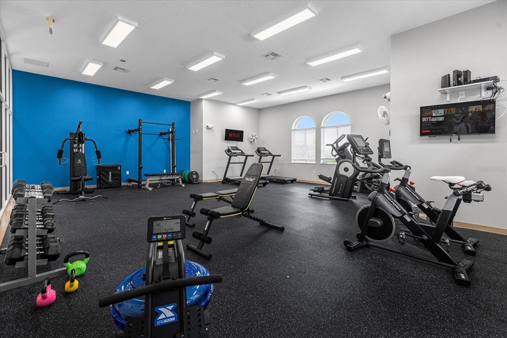 A gym room features rubber flooring, various exercise machines, free weights, and a wall-mounted television — 2306 LANCASHIRE STREET, DAVENPORT, FL