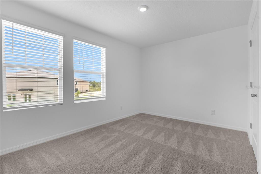 An empty bedroom features white walls, gray carpet, and two windows with white blinds — 2306 LANCASHIRE STREET, DAVENPORT, FL