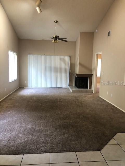 A living room features beige walls, brown carpeting, a ceiling fan, and a corner fireplace — 467 NEWTON PLACE, LONGWOOD, FL