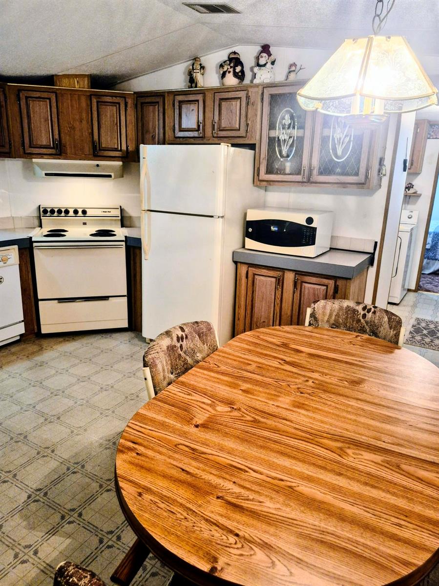 A kitchen features wood cabinets, white appliances, a round dining table, and patterned linoleum flooring — 1066 Peach Lane, Okeechobee FL 34974, OKEECHOBEE, FL