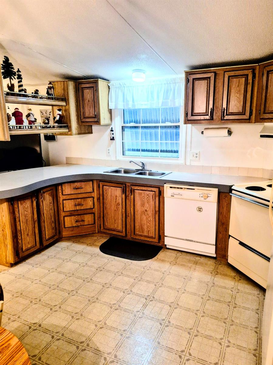 A kitchen features wood cabinets, a white dishwasher, a white stove, and light-colored flooring — 1066 Peach Lane, Okeechobee FL 34974, OKEECHOBEE, FL