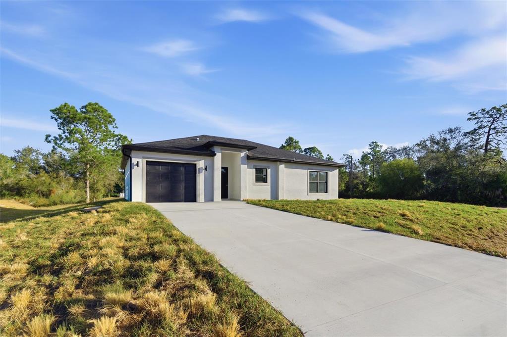 A single-story house with a concrete driveway, a dark garage door, and a white exterior — 107 E 15TH STREET, LEHIGH ACRES, FL