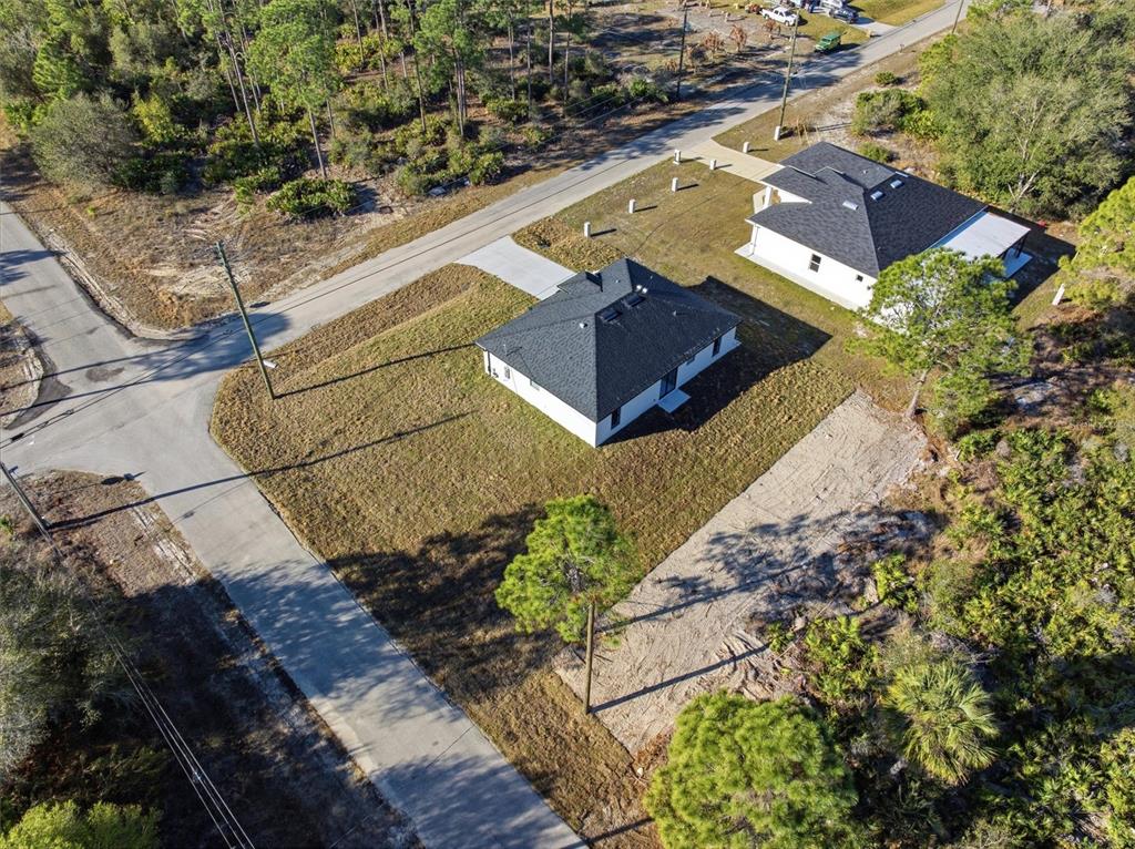 An aerial view shows two newly constructed houses on a corner lot with paved roads — 107 E 15TH STREET, LEHIGH ACRES, FL