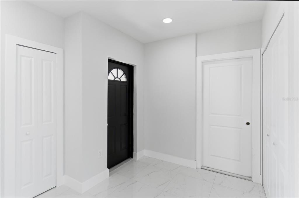 A bright entryway features white walls, marble-look tile flooring, and a black front door — 107 E 15TH STREET, LEHIGH ACRES, FL