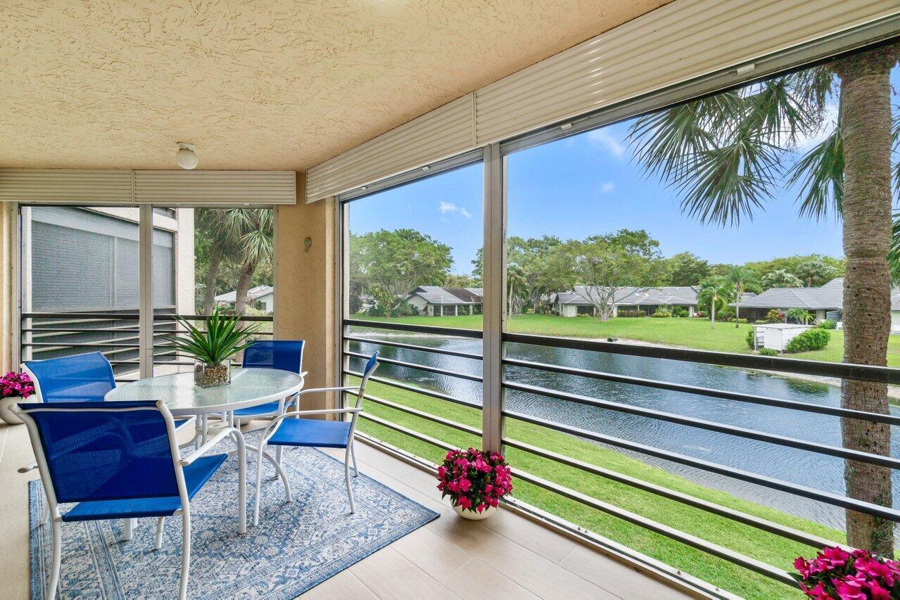 A screened-in balcony features a dining set, tile flooring, and a view of a pond — 10092 Cedar Point Boulevard # 204, Boynton Beach FL 33437, BOYNTON BEACH, FL