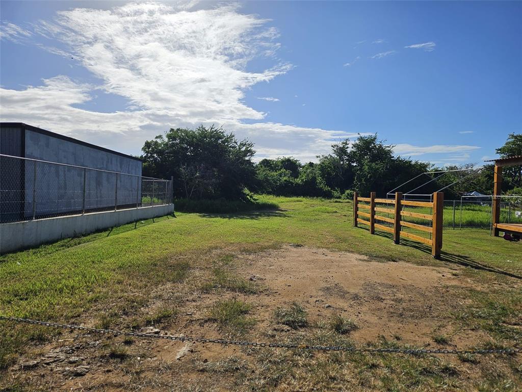 A grassy lot features a chain-link fence, a wooden gate, and a metal storage building — SOLAR EN BO.CIBAO, CAMUY, PR