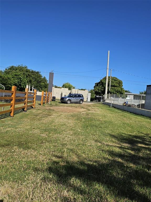 A grassy lot features a wooden fence on the left and a parked SUV — SOLAR EN BO.CIBAO, CAMUY, PR