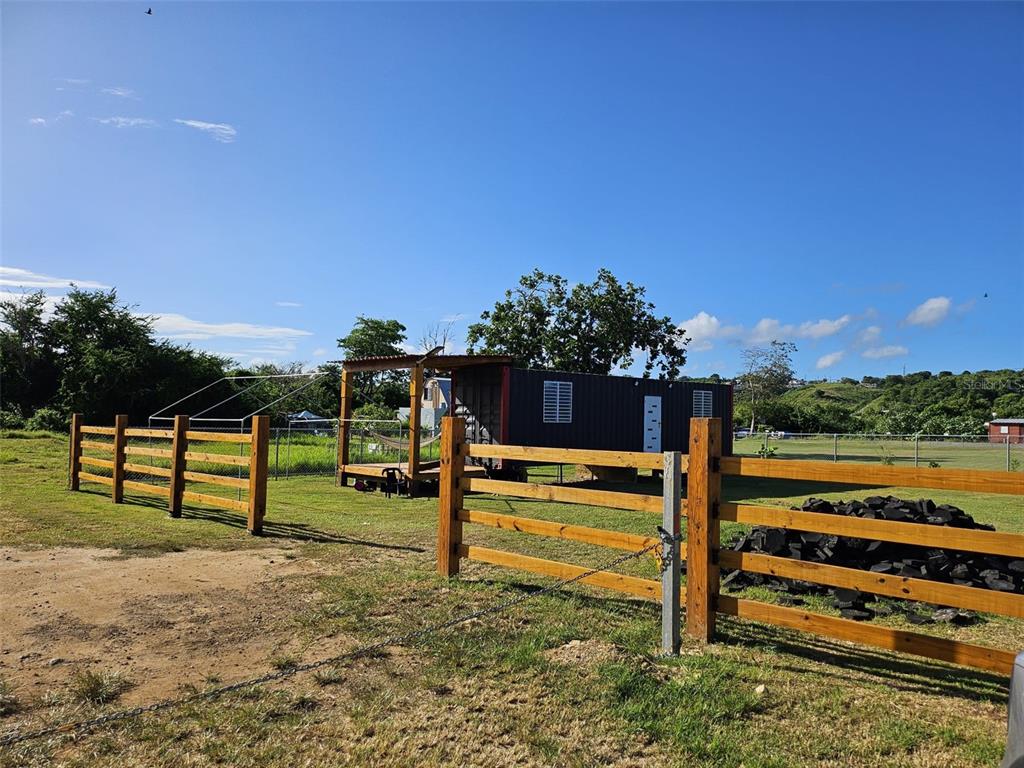 A shipping container home sits on a grassy lot behind a wooden fence — SOLAR EN BO.CIBAO, CAMUY, PR