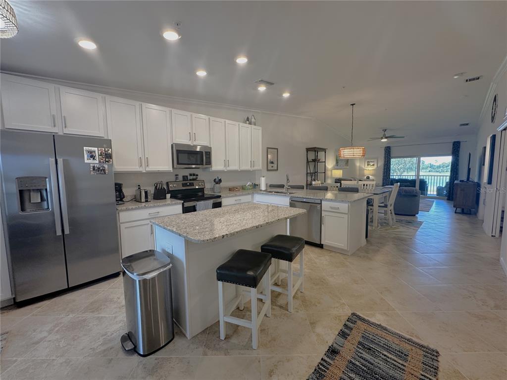 A kitchen with white cabinets, granite countertops, and a center island opens to a living area — 14050 HERITAGE LANDING BOULEVARD UNIT 225, PUNTA GORDA, FL