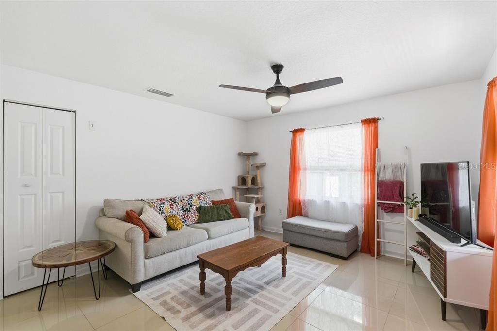A living room features a beige sofa, wooden coffee table, television, and orange window curtains — 950 S PARSONS AVENUE, DELAND, FL
