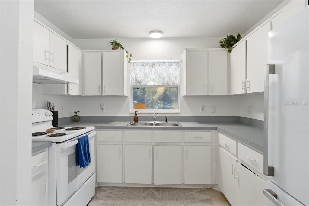 A kitchen features white cabinets, gray countertops, a white stove, and a window above the sink — 950 S PARSONS AVENUE, DELAND, FL