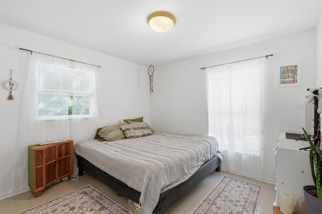 A bedroom features a bed with striped bedding, two windows with white curtains, and tile flooring — 950 S PARSONS AVENUE, DELAND, FL