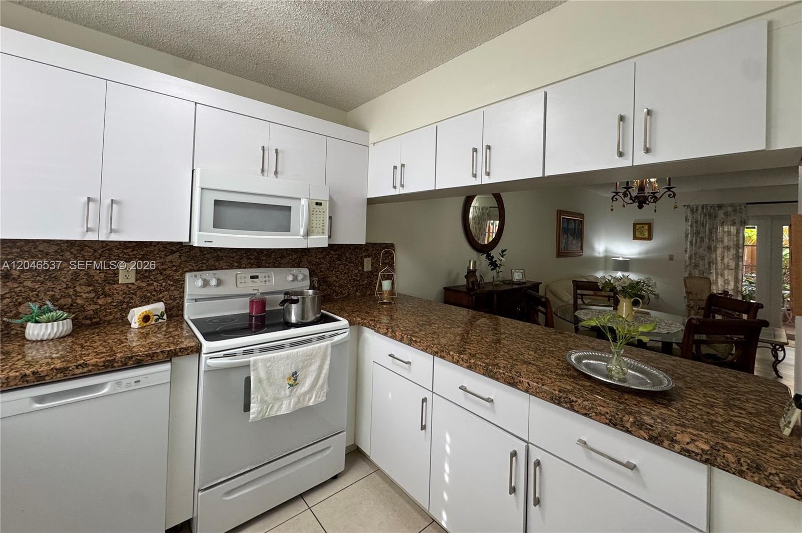 A kitchen features white cabinets, granite countertops, and a white stove with a microwave above — 2365 W 74th St, Hialeah FL 33016, HIALEAH, FL