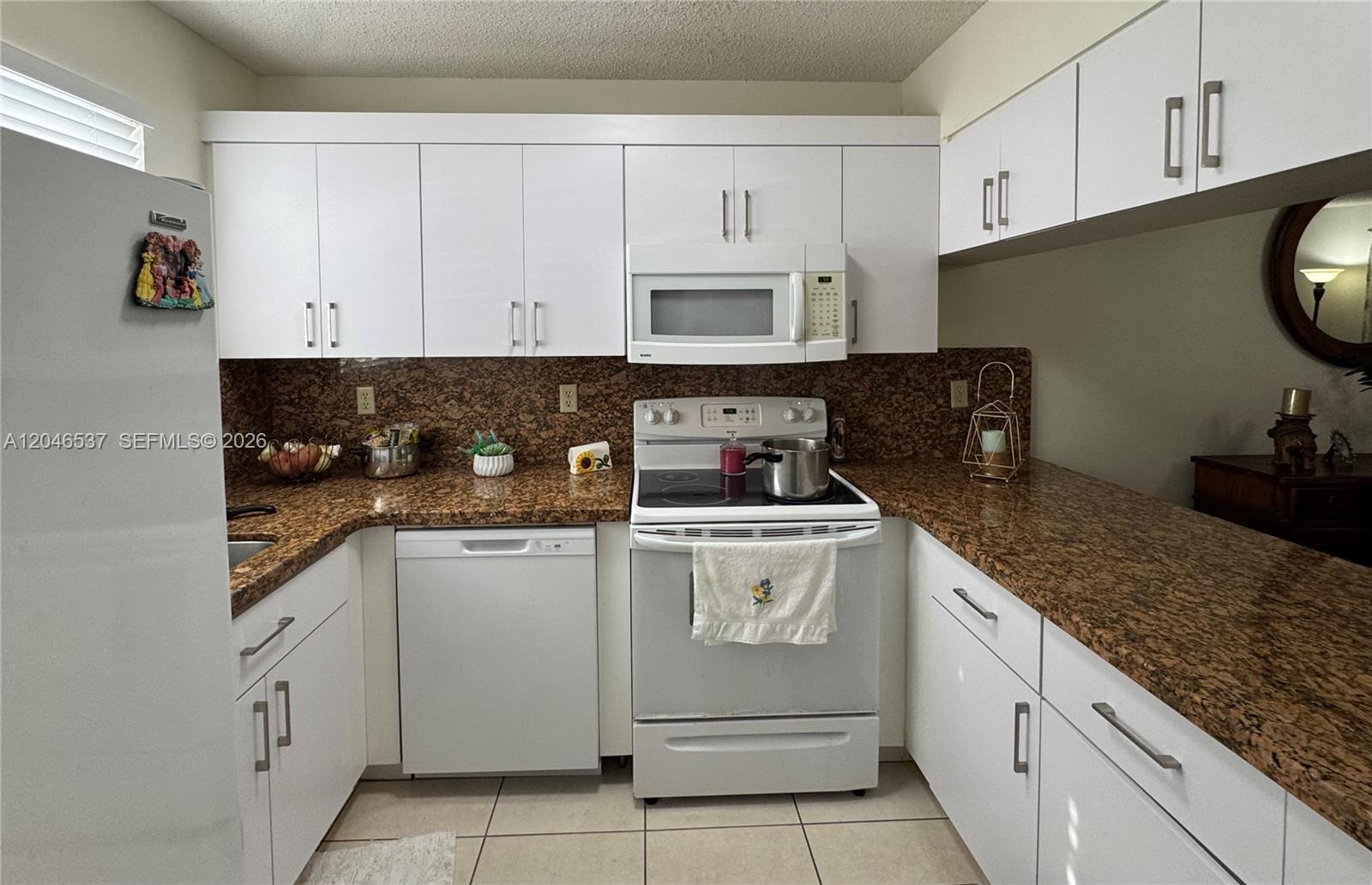 A kitchen features white cabinets, brown granite countertops, and white appliances — 2365 W 74th St, Hialeah FL 33016, HIALEAH, FL