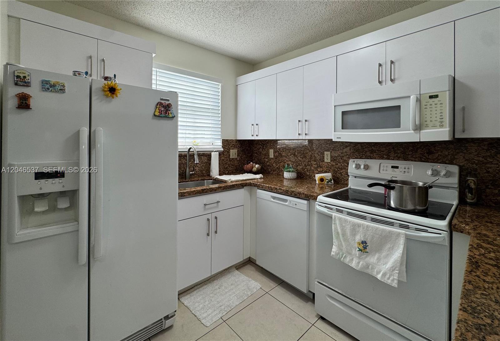 A kitchen features white cabinets, granite countertops, white appliances, and a tiled floor — 2365 W 74th St, Hialeah FL 33016, HIALEAH, FL