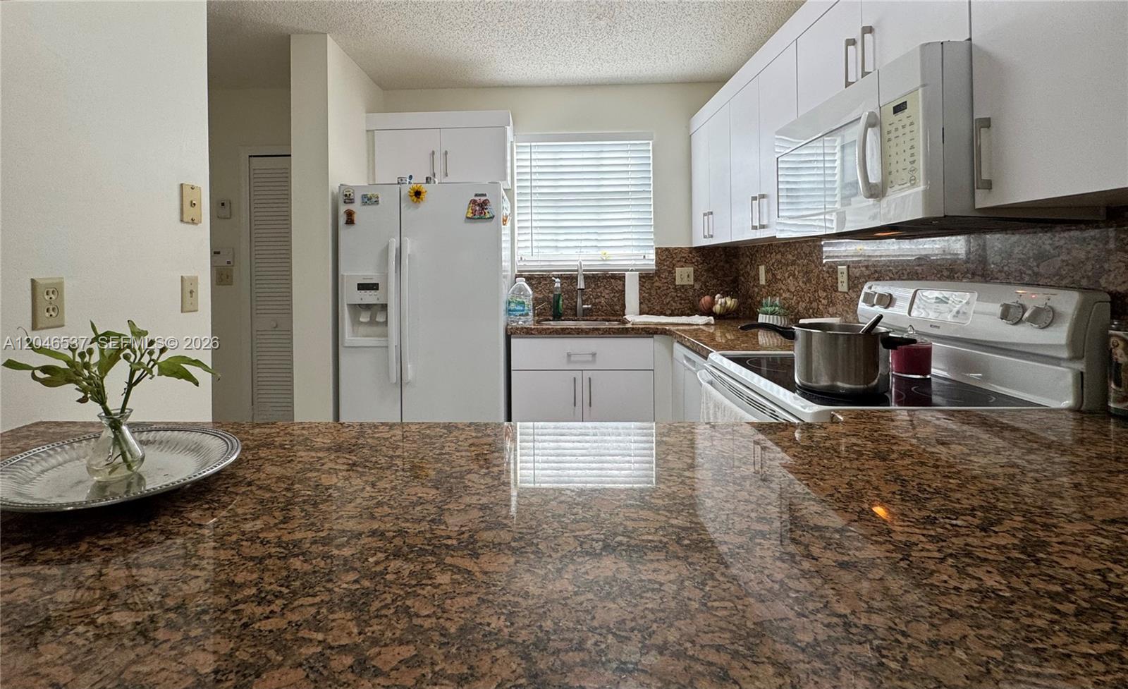 A kitchen features white cabinets, brown granite countertops, and a white refrigerator — 2365 W 74th St, Hialeah FL 33016, HIALEAH, FL