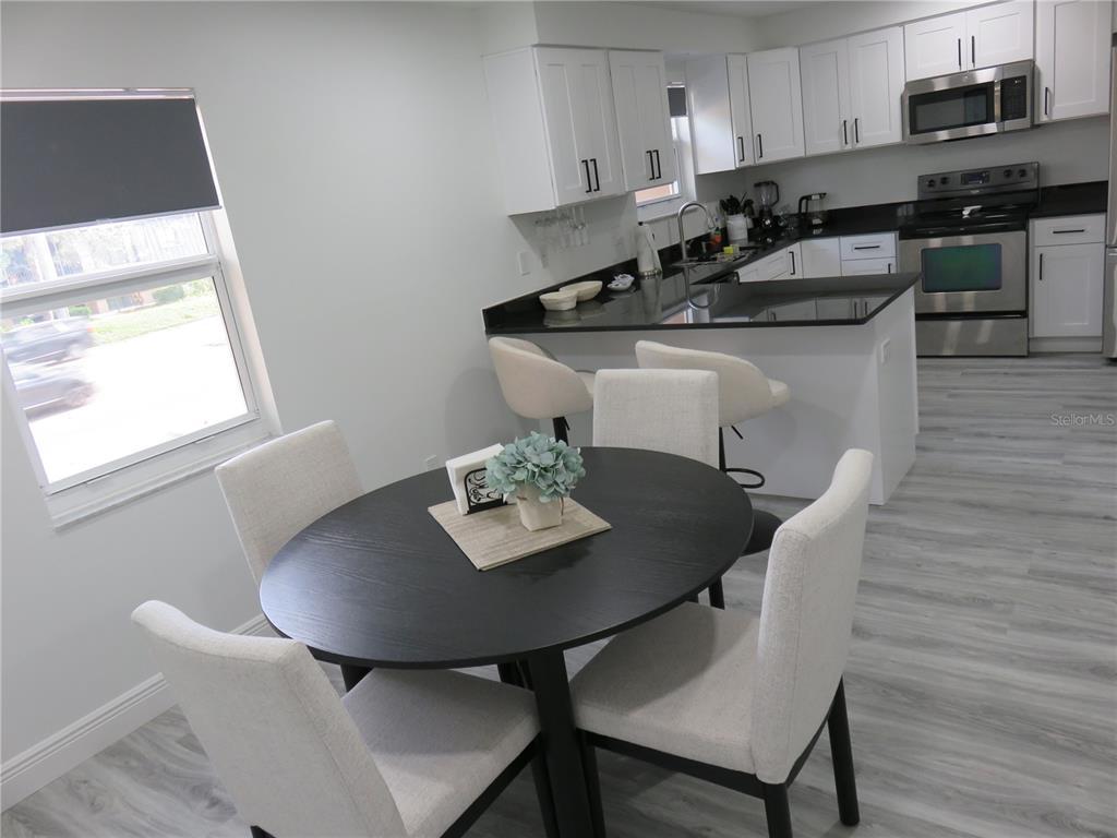 A dining area with a round table sits adjacent to a kitchen with white cabinets — 5401 SWEETWATER TERRACE CIRCLE UNIT 5401, TAMPA, FL