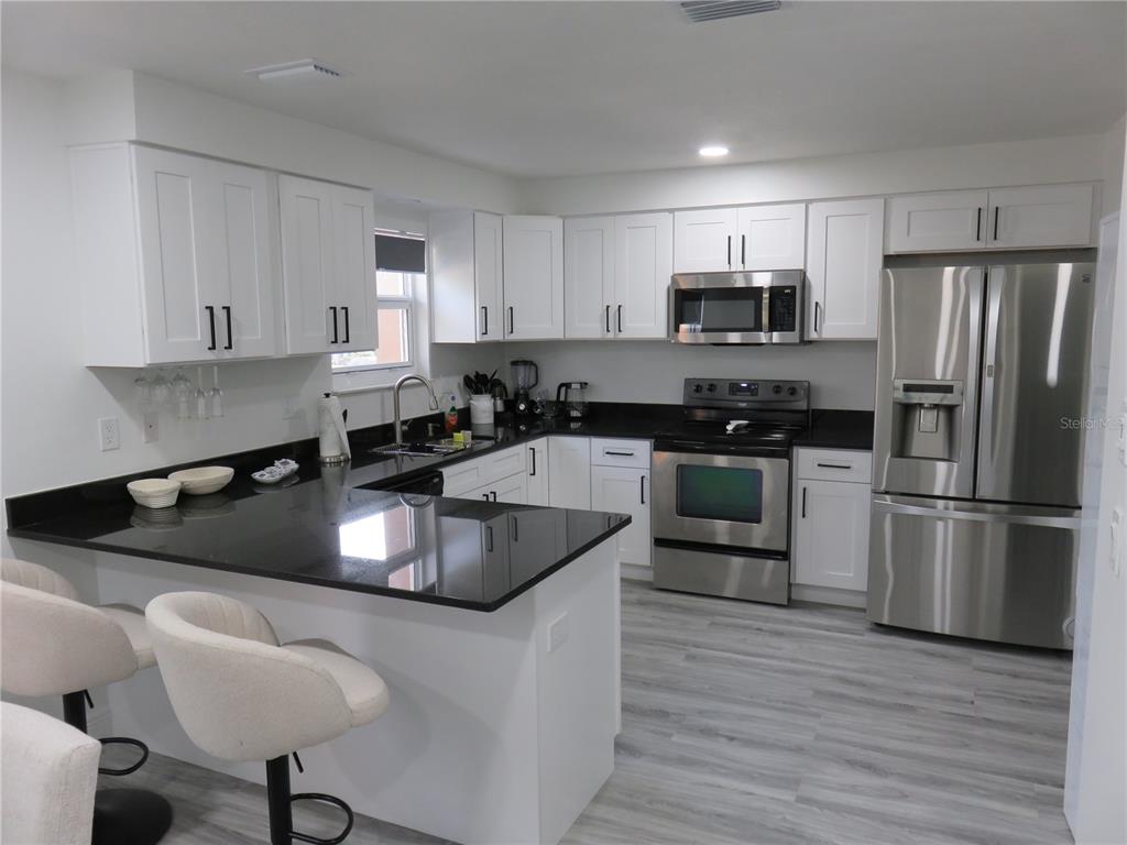 A modern kitchen features white cabinets, black countertops, stainless steel appliances, and a breakfast bar — 5401 SWEETWATER TERRACE CIRCLE UNIT 5401, TAMPA, FL