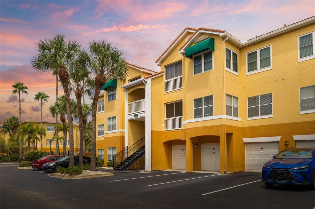 A three-story yellow apartment building with attached garages and palm trees in the parking lot — 10764 70TH AVENUE UNIT 1304, SEMINOLE, FL