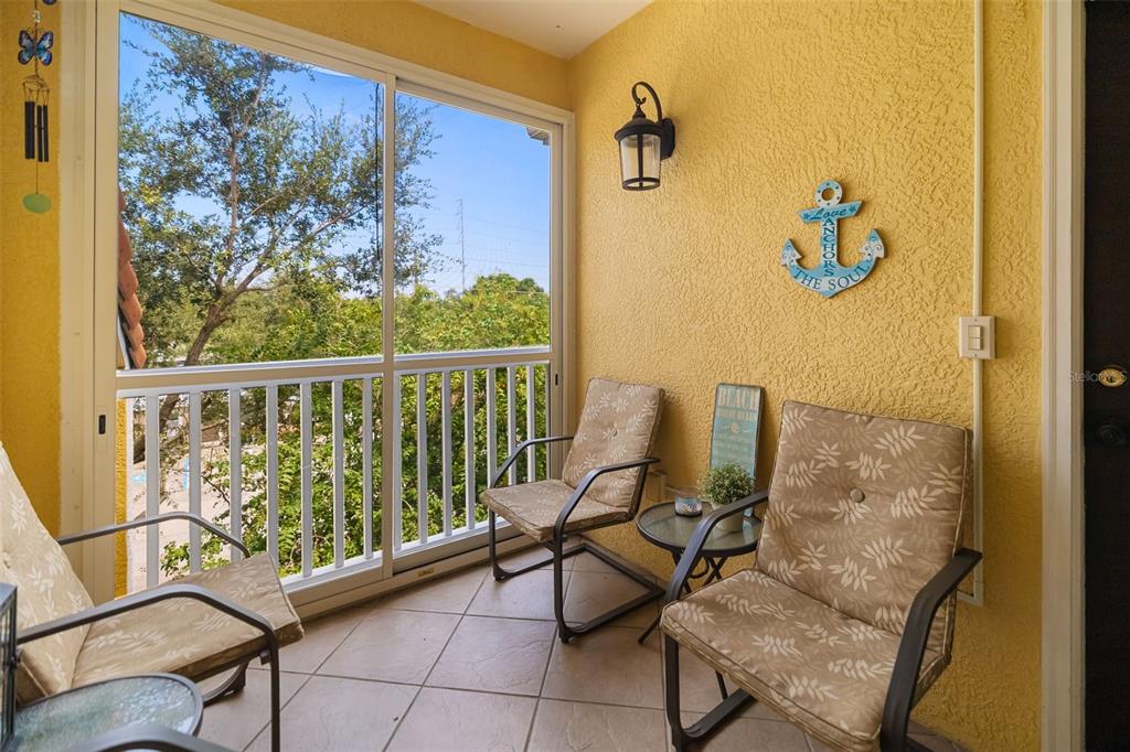 A screened-in balcony features yellow walls, tiled flooring, three chairs, and a small table — 10764 70TH AVENUE UNIT 1304, SEMINOLE, FL