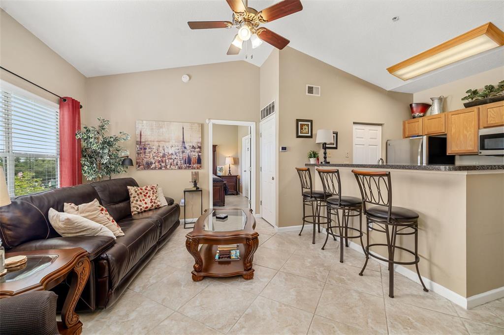 A living room with a brown leather sofa, coffee table, and breakfast bar with stools — 10764 70TH AVENUE UNIT 1304, SEMINOLE, FL