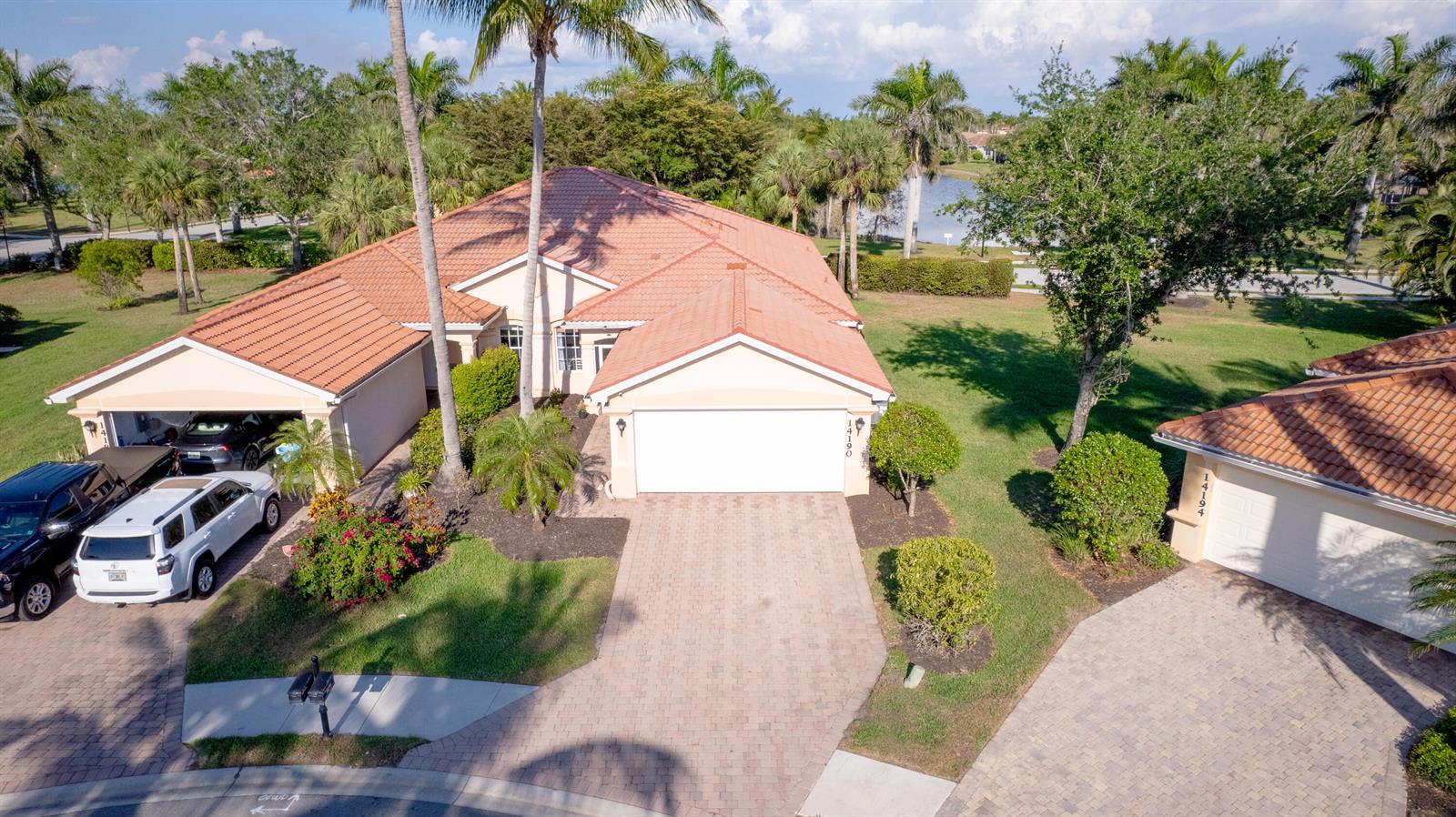An aerial view shows two houses with terracotta-tiled roofs and paved driveways in a neighborhood — 14190 Fall Creek Court, Naples FL 34114, NAPLES, FL