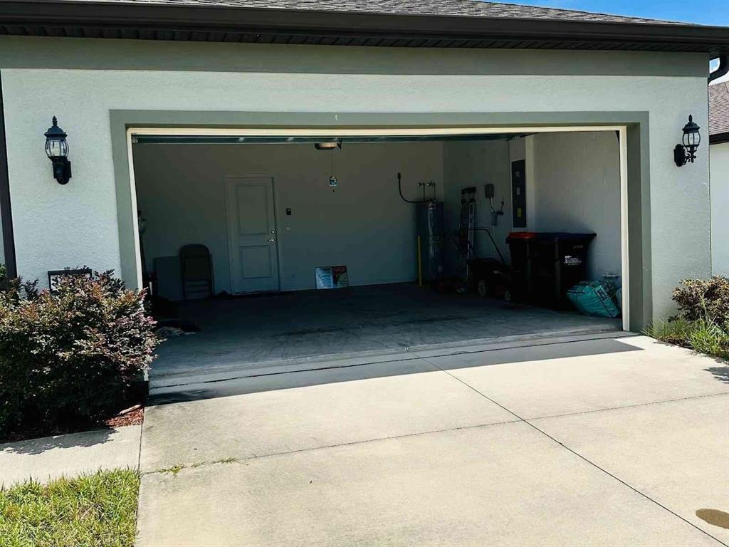 An open garage with a concrete floor, a side door, and a water heater inside — 9335 SW 53RD PLACE, OCALA, FL
