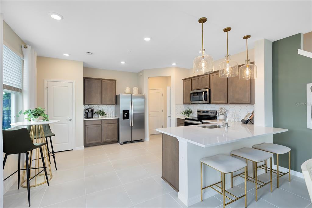 A modern kitchen features white countertops, stainless steel appliances, and a breakfast bar with stools — 3234 PONDSIDE WAY, SANFORD, FL