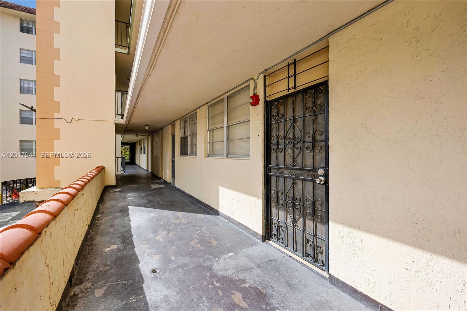 An outdoor apartment walkway features a metal security door and a low stucco wall — 12590 NE 16th Ave # 208, North Miami FL 33161, NORTH MIAMI, FL