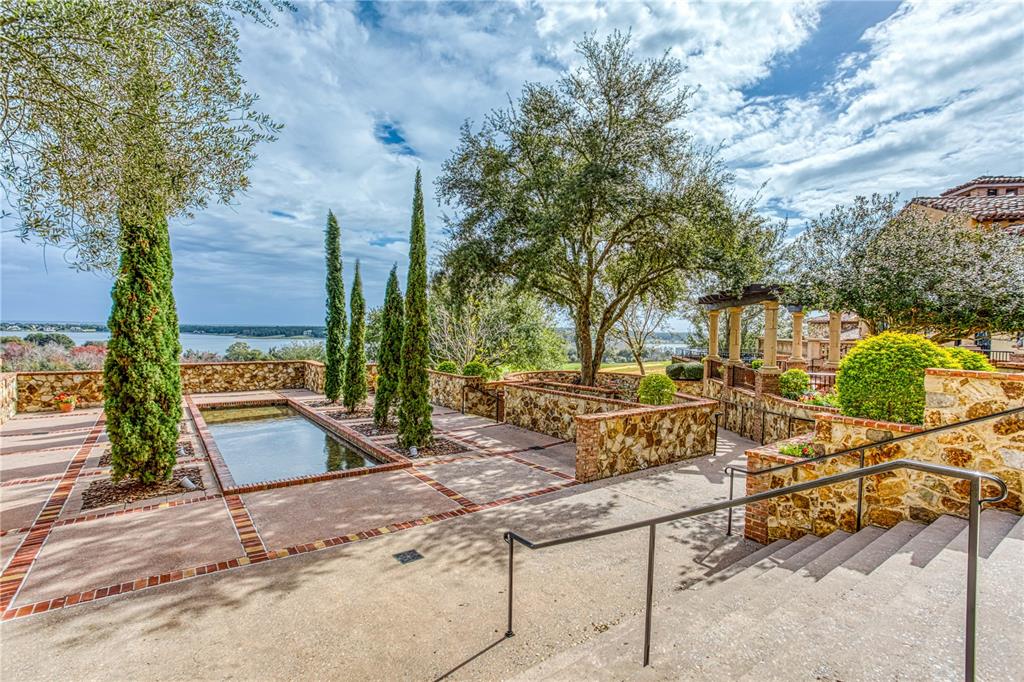 A stone patio features a rectangular reflecting pool, tall cypress trees, and a scenic lake view — 17114 MEDICI WAY, BELLA COLLINA, FL