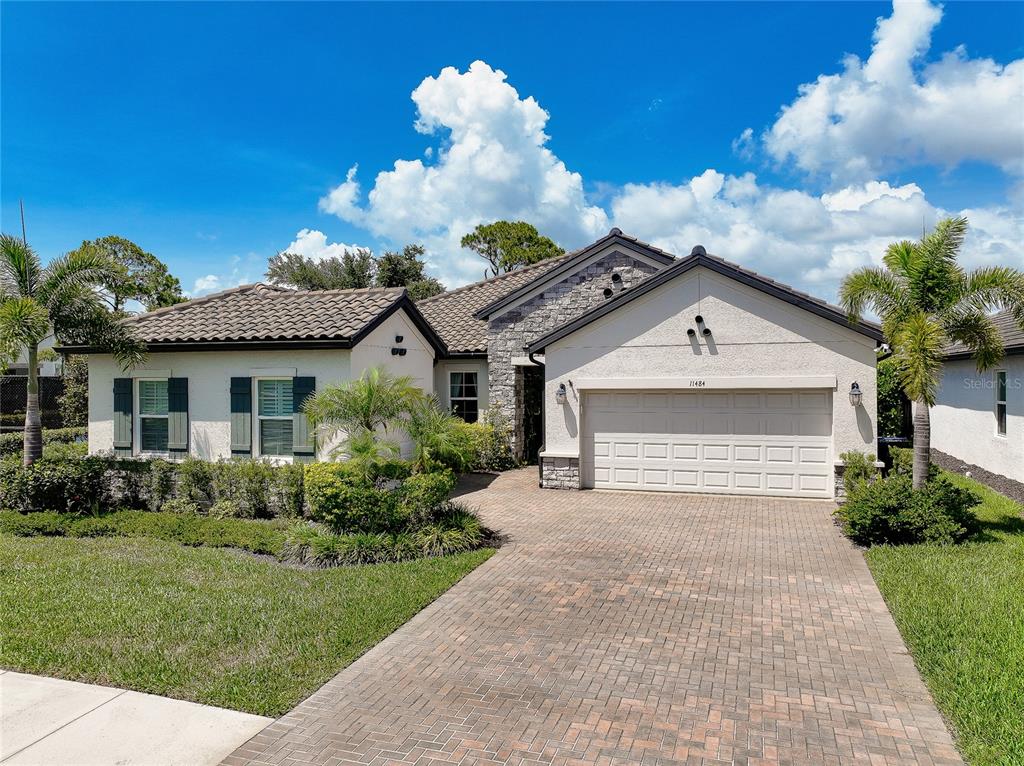 A single-story house with a stone facade, a two-car garage, and a brick paver driveway — 11484 MONTSERRAT DRIVE, VENICE, FL