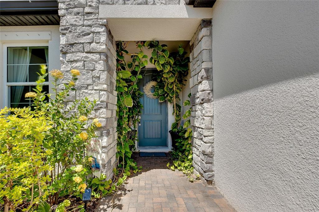 A stone-accented entryway features a blue front door surrounded by climbing vines and greenery — 11484 MONTSERRAT DRIVE, VENICE, FL