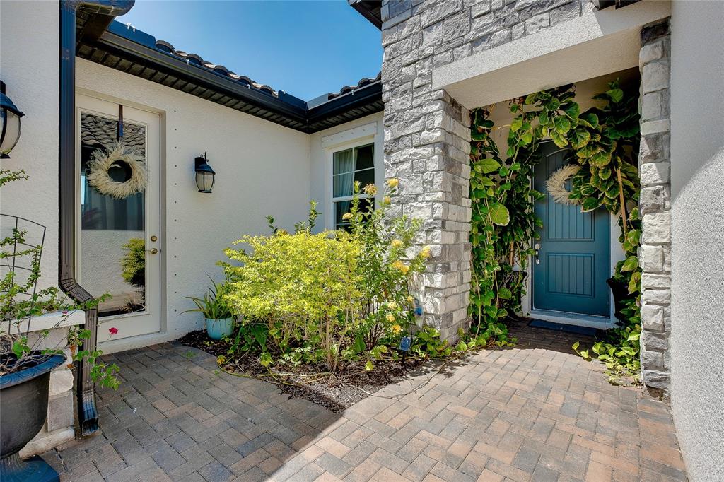 A stone-accented entryway features a blue front door, a side door, and a paved patio — 11484 MONTSERRAT DRIVE, VENICE, FL