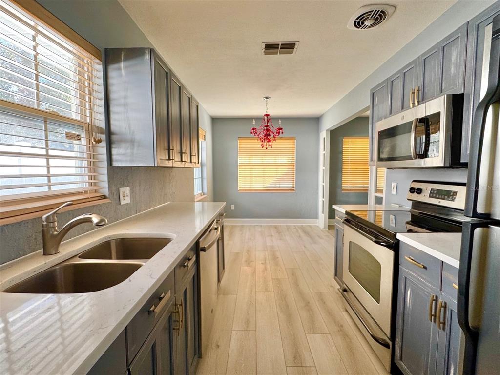 A galley kitchen features dark blue cabinets, stainless steel appliances, and light wood-look flooring — 185 22ND AVENUE N, ST PETERSBURG, FL