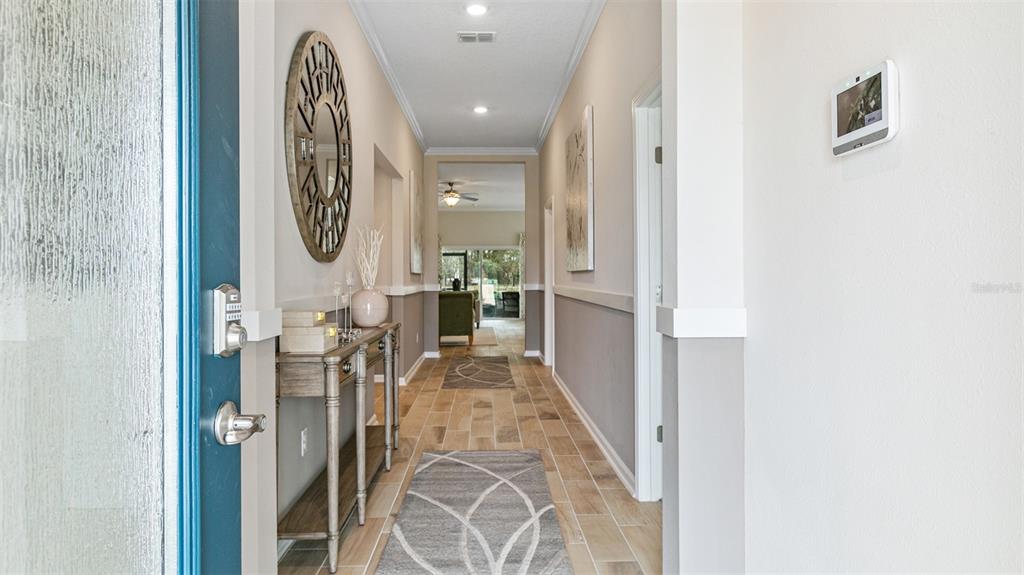 A bright entryway features a console table, a round wall mirror, and tile flooring — 46 HARDWOOD TRAIL, PALM COAST, FL
