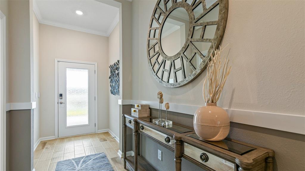 A foyer features a console table, a large circular mirror, and a white front door — 46 HARDWOOD TRAIL, PALM COAST, FL