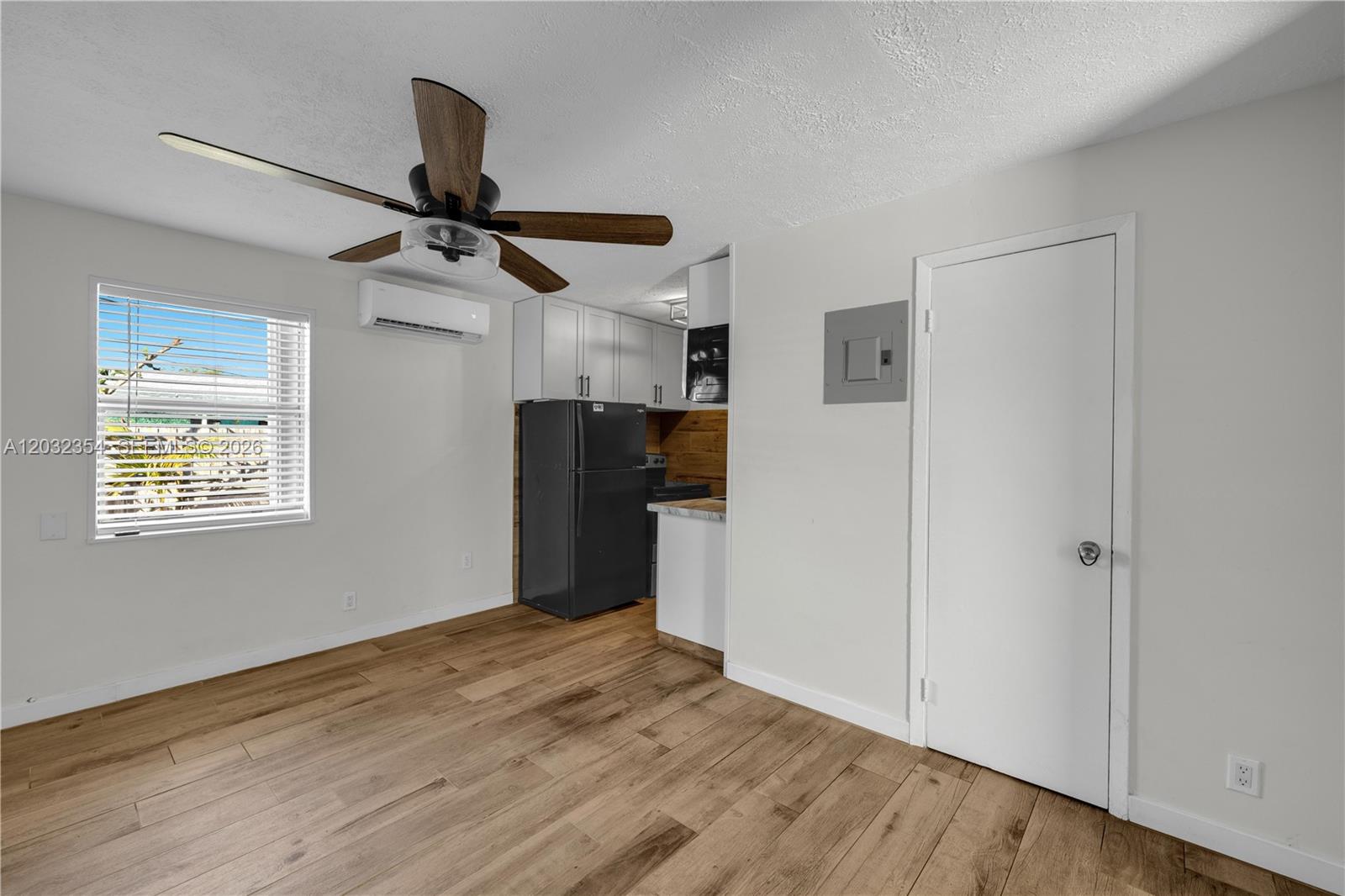 A room with wood-look flooring, a ceiling fan, a kitchen area, and a white door — HOLLYWOOD, FL