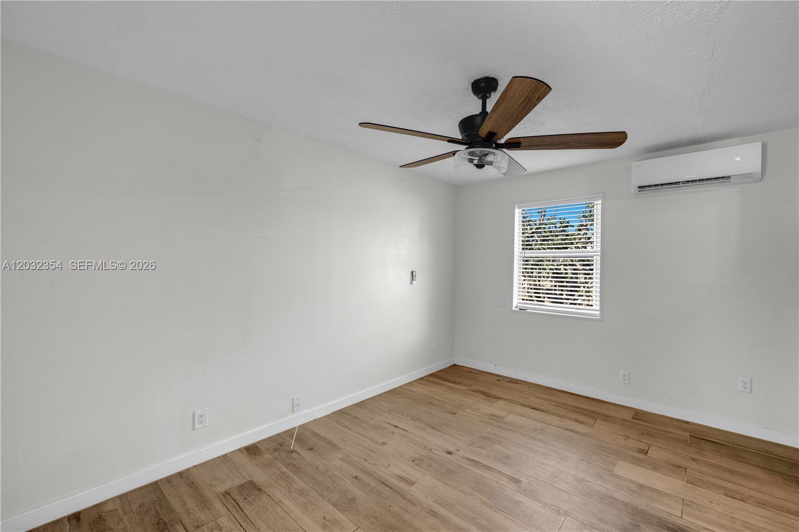 An empty bedroom features light wood-look flooring, a ceiling fan, and a wall-mounted air conditioner — HOLLYWOOD, FL