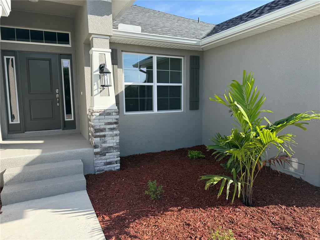 The exterior of a house features a gray front door, stone pillar, and palm tree — 9527 IMPALA CIRCLE, PORT CHARLOTTE, FL